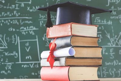 libri in pila con sopra un cappello di laurea e sullo sfondo una lavagna con numeri e formule matematiche