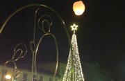 immagine della notte delle lanterne: una lanterna in cielo e sullo sfondo l'albero di natale illuminato